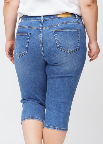 Tæt billede af bagdelen på en plus-size model i blå denim slim capris – detaljefokus på lommer og syninger.
