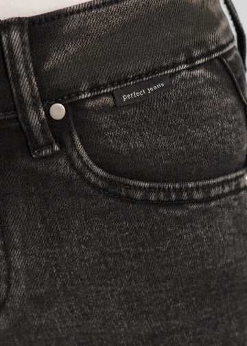 Nærbillede af mørkegrå denim med Perfect Jeans logoetiket ved forlommekanten.
