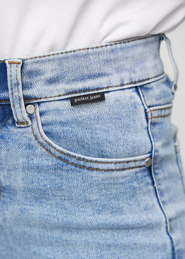 Nærbillede af lyseblå denim med Perfect Jeans logoetiket ved forlommekanten.