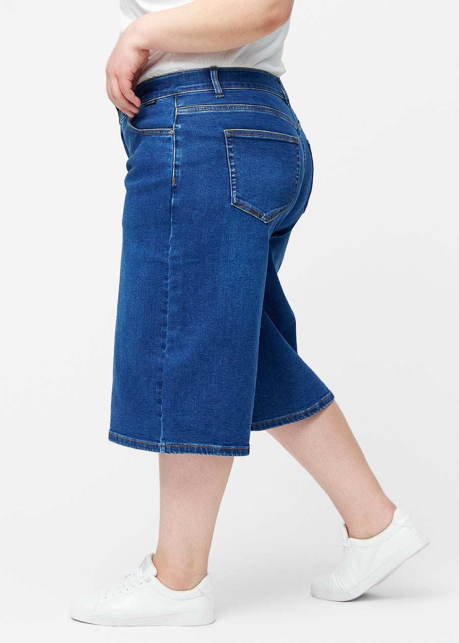 Løse, mørkeblå denim capris i farven Oceans set fra siden på plus-size model, hvor den brede pasform og længden til lige under knæet er synlig.