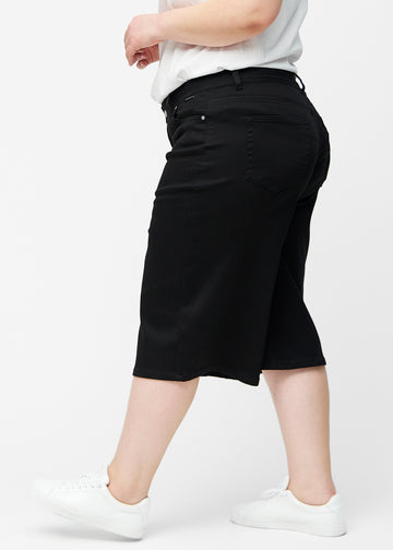 Løse, sorte capris i farven Ravens set fra siden på plus-size model, hvor den brede pasform og længden til lige under knæet er synlig.