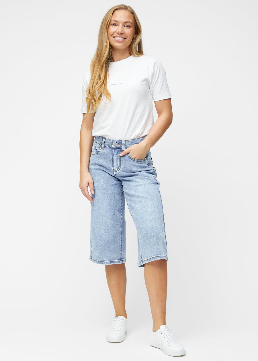 Fuldt billede af model i løse, lyseblå denim capris i farven Waves, der går til lige under knæet.