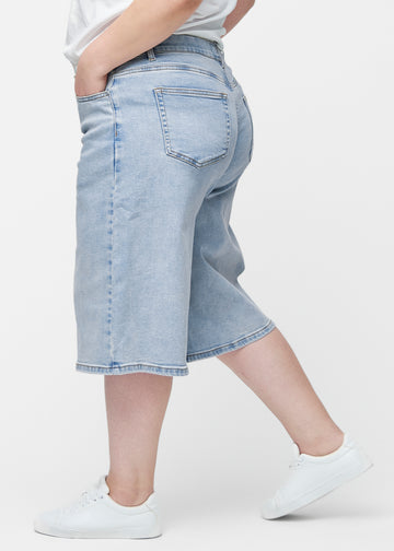 Løse, lyseblå denim capris i farven Waves set fra siden på plus-size model, hvor den brede pasform og længden til lige under knæet er synlig.