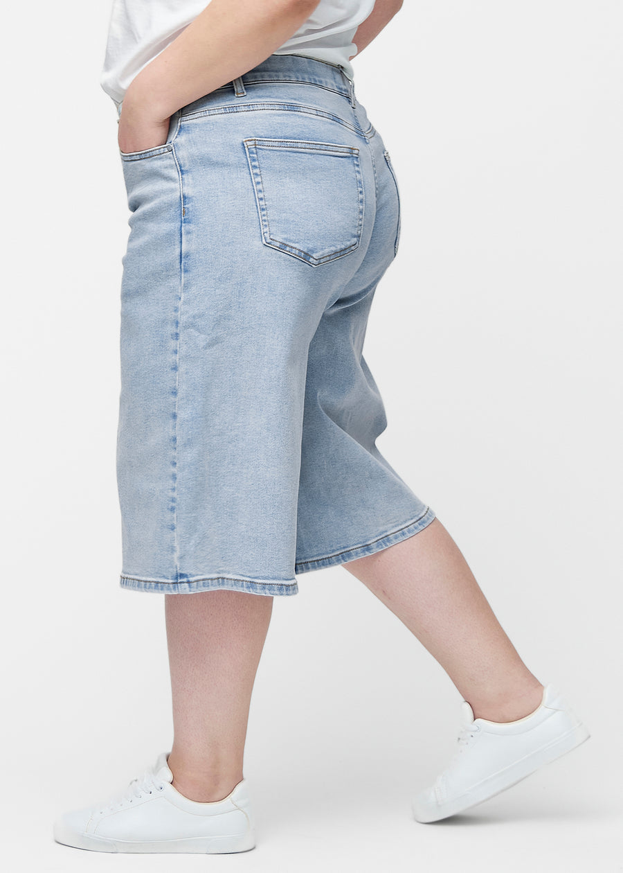 Løse, lyseblå denim capris i farven Waves set fra siden på plus-size model, hvor den brede pasform og længden til lige under knæet er synlig.