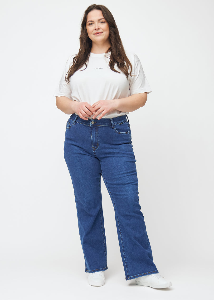 Fuldt billede af en plus-size model i mørkeblå mid-rise bootcut jeans i denimfarven Oceans.