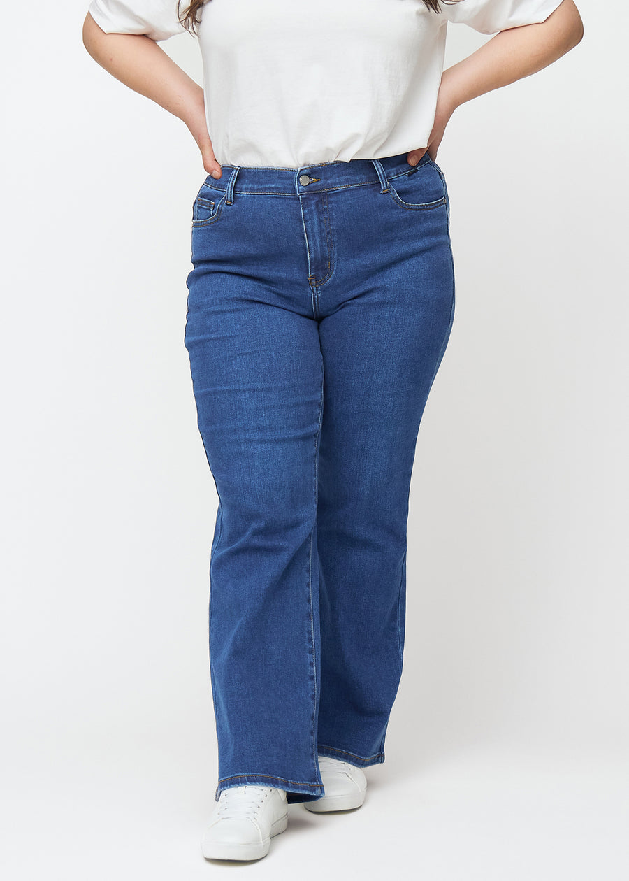 Mørkeblå mid-rise bootcut jeans i denimfarven Oceans, som sidder tæt fra hofte til lår og har et let svaj forneden, på en plus-size model, set forfra.