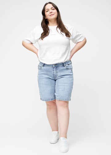 Fuldt billede af plus-size model i løse, lyseblå denim shorts i farven Waves, der går til lige over knæet.