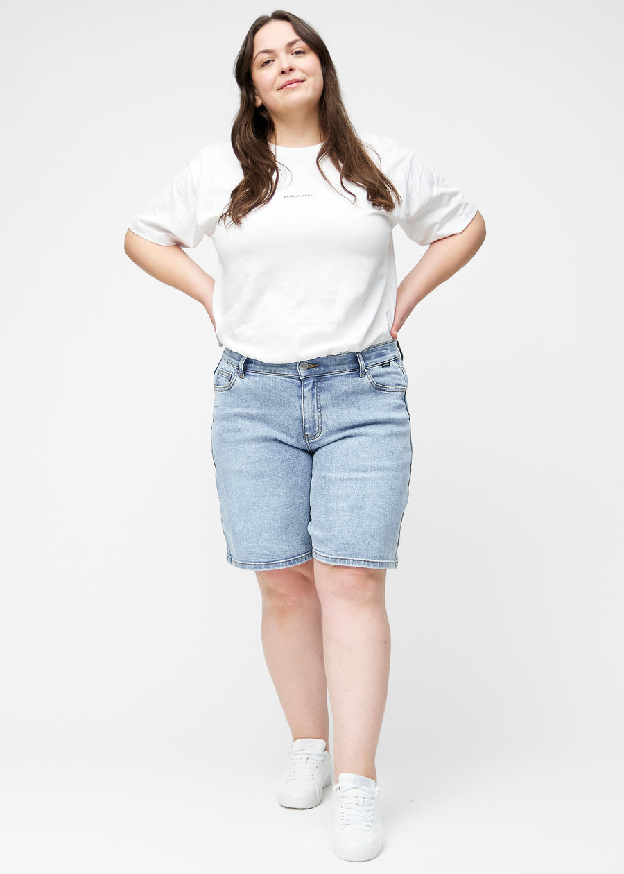 Fuldt billede af plus-size model i løse, lyseblå denim shorts i farven Waves, der går til lige over knæet.
