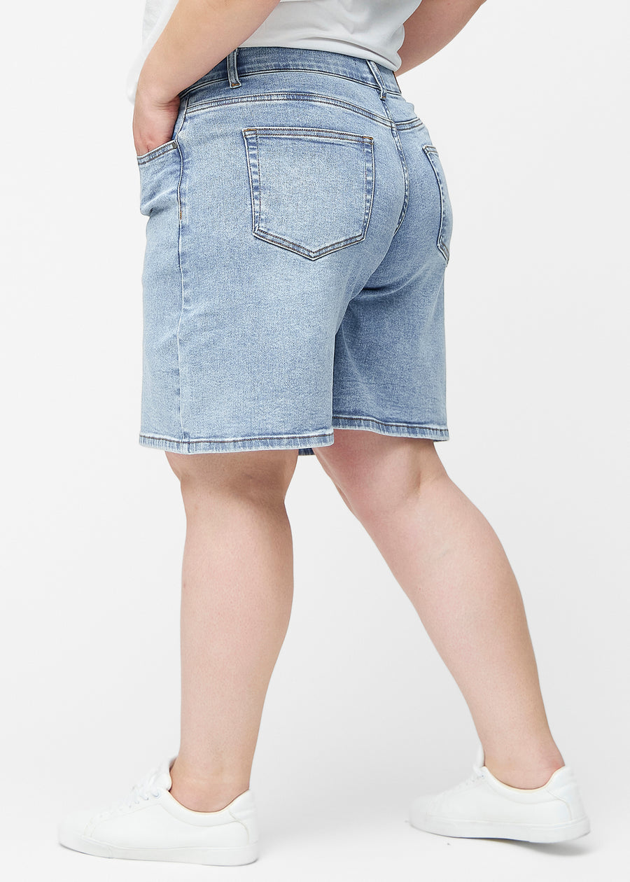 Løse, lyseblå denim shorts i farven Waves set fra siden på plus-size model, hvor den brede pasform og længden til lige over knæet er synlig.