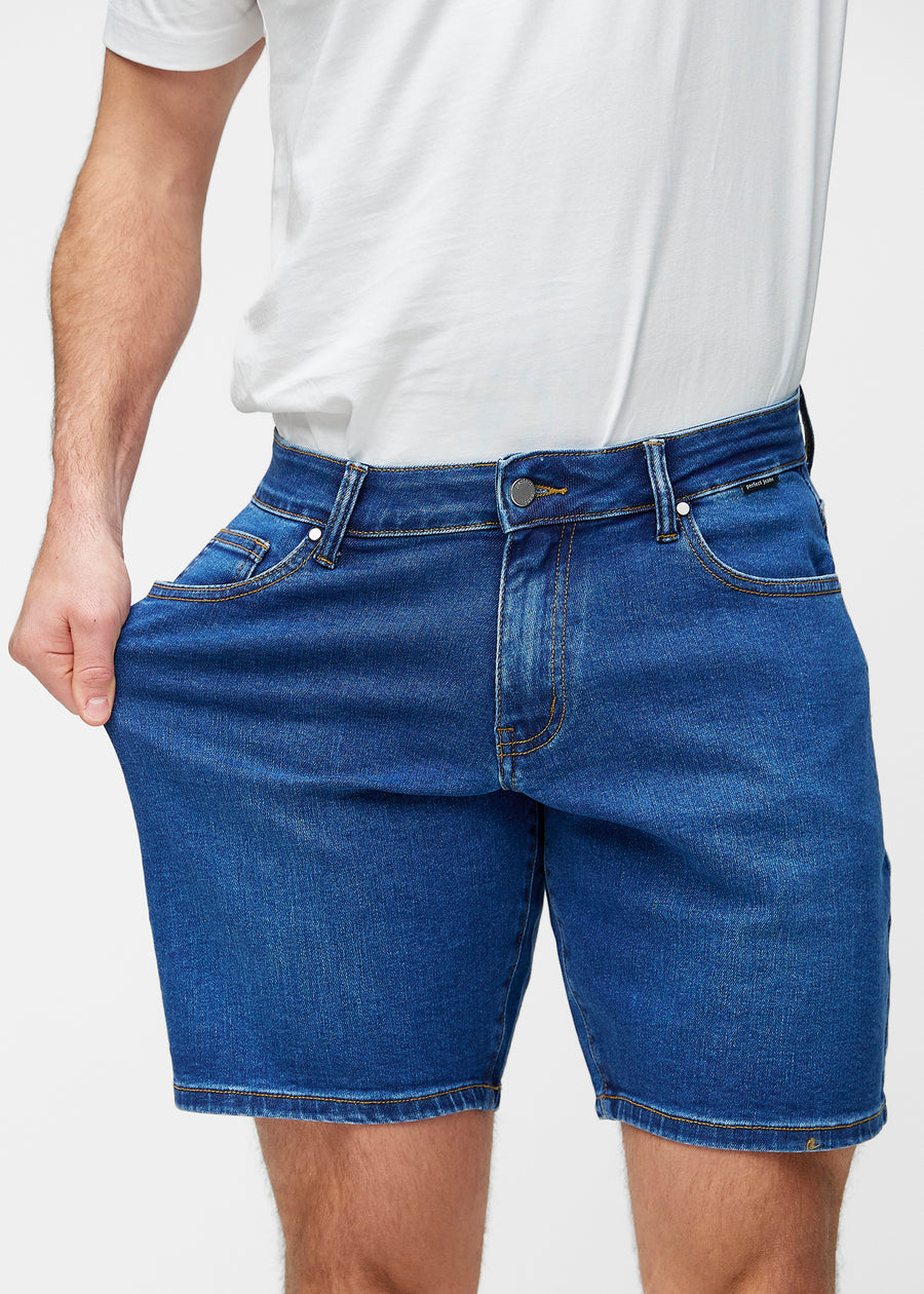 Model strækker mørkeblå denim shorts til mænd i farven Oceans ved låret for at vise materialets stretch.