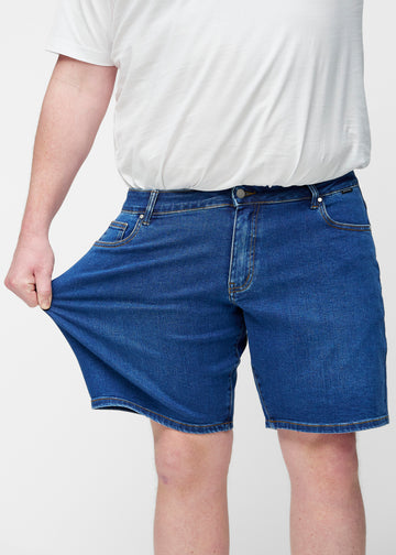 Plus-size model strækker mørkeblå denim shorts til mænd i farven Oceans ved låret for at vise materialets stretch.
