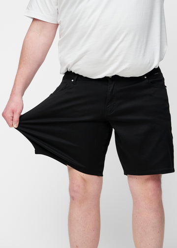 Plus-size model strækker sorte shorts til mænd i farven Ravens ved låret for at vise materialets stretch.