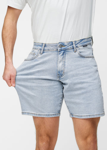 Model strækker lyseblå denim shorts til mænd i farven Waves ved låret for at vise materialets stretch.