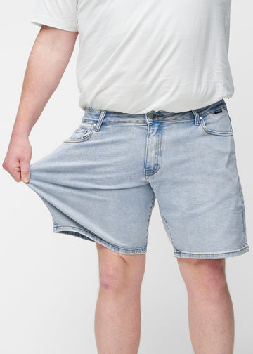 Plus-size model strækker lyseblå denim shorts til mænd i farven Waves ved låret for at vise materialets stretch.