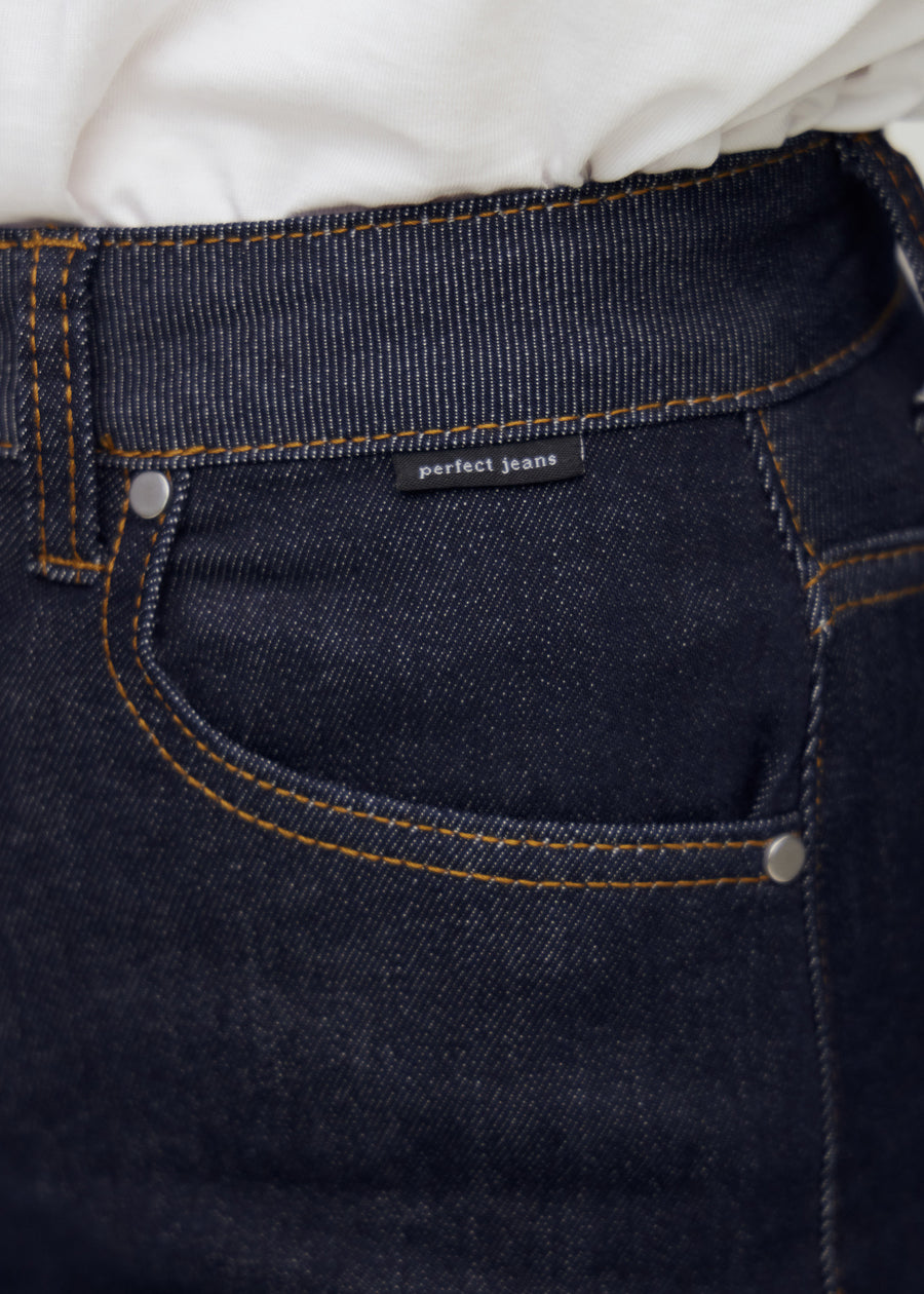 Nærbillede af dyb mørkeblå denim med Perfect Jeans logoetiket ved forlommekanten.