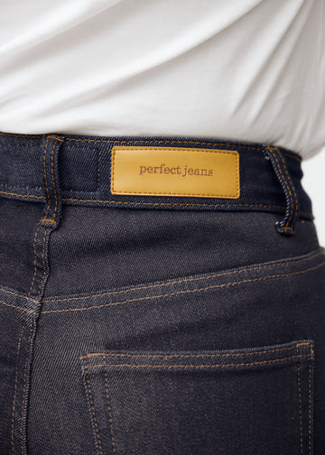Nærbillede af dyb mørkeblå denim med Perfect Jeans læderpatch bagpå i taljen.