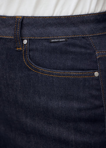 Nærbillede af dyb mørkeblå denim med Perfect Jeans logoetiket ved forlommekanten, på en plus-size model.
