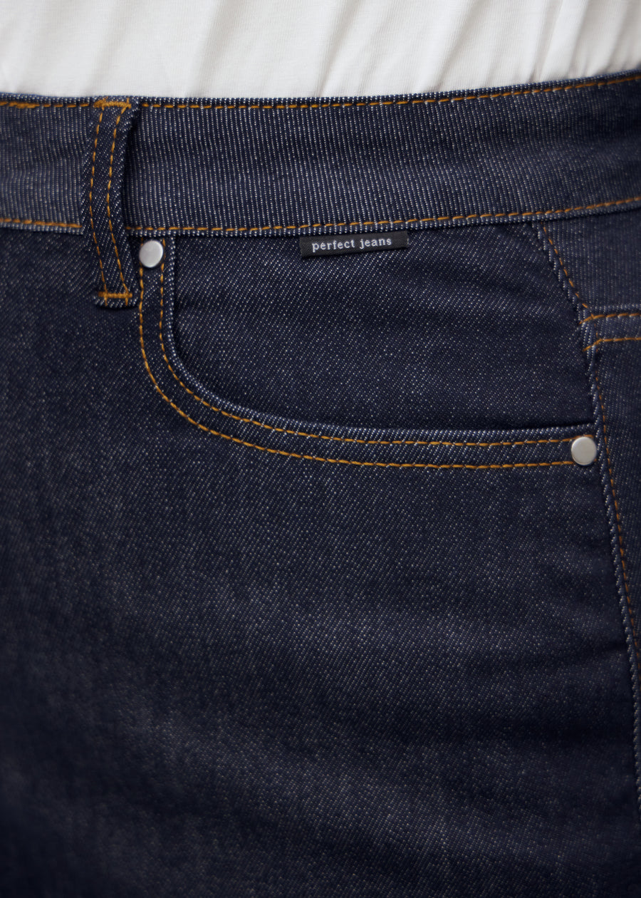 Nærbillede af dyb mørkeblå denim med Perfect Jeans logoetiket ved forlommekanten, på en plus-size model.