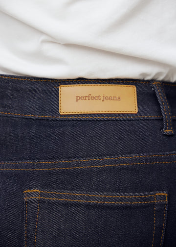 Nærbillede af dyb mørkeblå denim med Perfect Jeans læderpatch bagpå i taljen, på en plus-size model.
