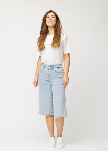 Fuldt billede af model i løse, lyseblå denim capris i farven Waves, der går til lige under knæet.

