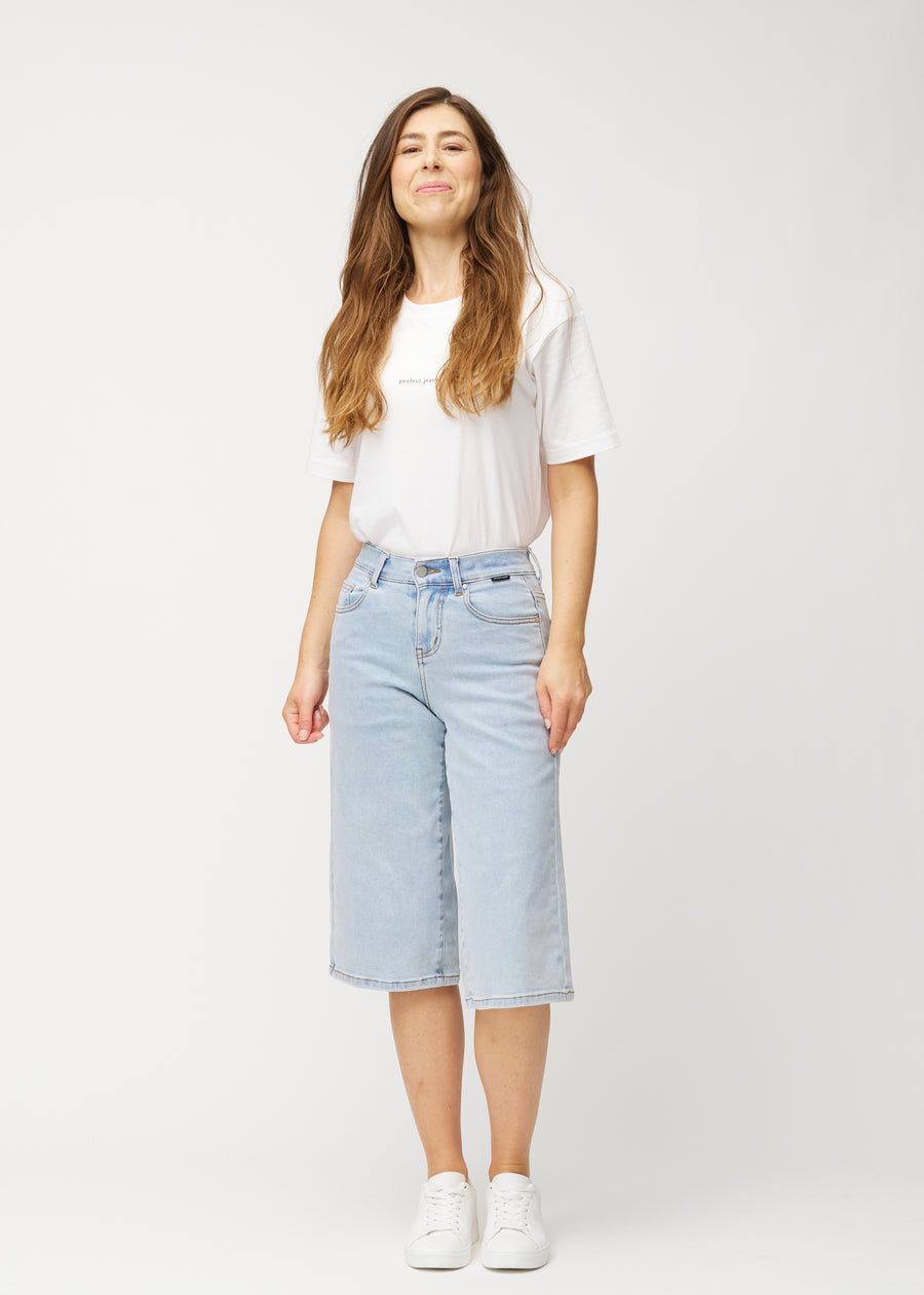 Fuldt billede af model i løse, lyseblå denim capris i farven Waves, der går til lige under knæet.
