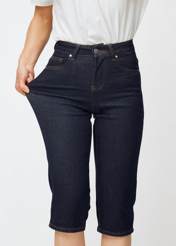 Model strækker dyb mørkeblå denim capris til kvinder i farven Midnights ved låret for at vise materialets stretch.