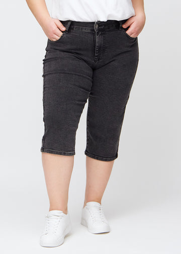 Mørkegrå denim regular capris, modelnavn Shadows, som sidder lige til benet og slutter lige under knæet på en plus-size model, set forfra.