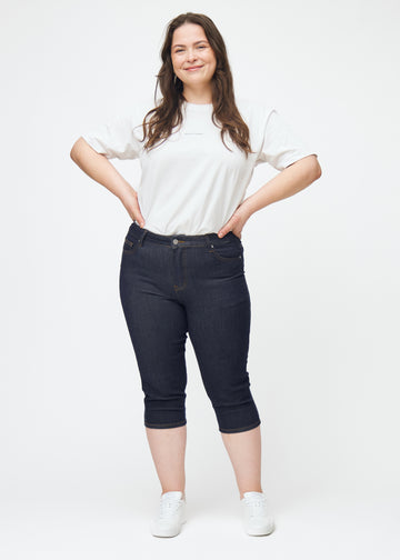 Fuldt billede af plus-size model i dyb mørkeblå denim capris til kvinder i farven Midnights med skinny pasform.