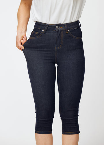 Model strækker dyb mørkeblå denim capris til kvinder i farven Midnights ved låret for at vise materialets stretch.