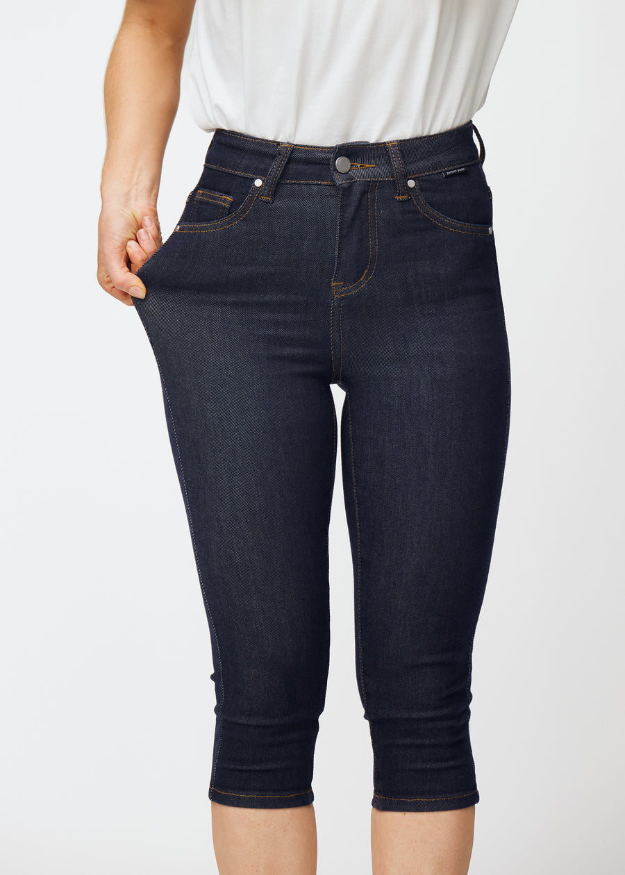 Model strækker dyb mørkeblå denim capris til kvinder i farven Midnights ved låret for at vise materialets stretch.