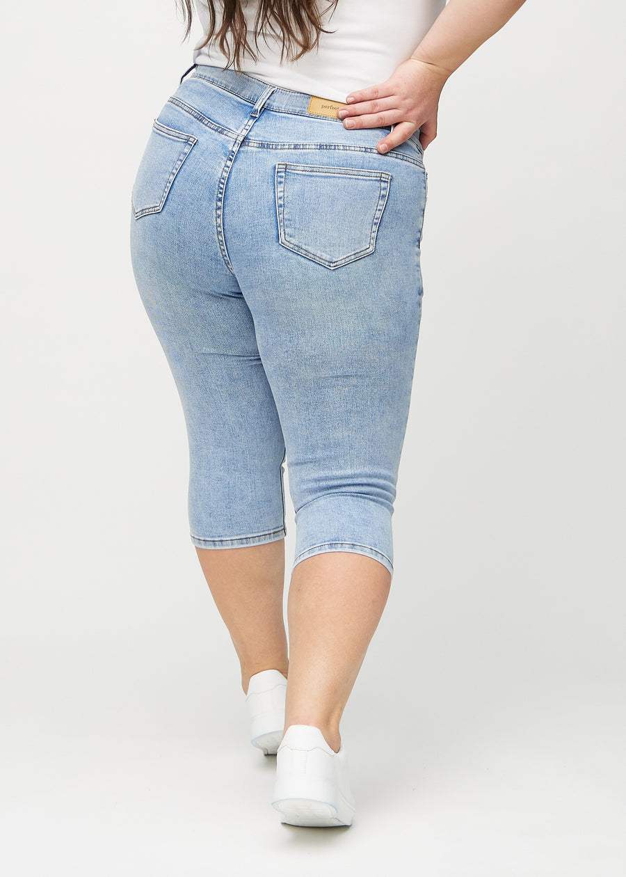 Lys denim skinny capris set bagfra på en plus-size model, så man kan se hele produktet.