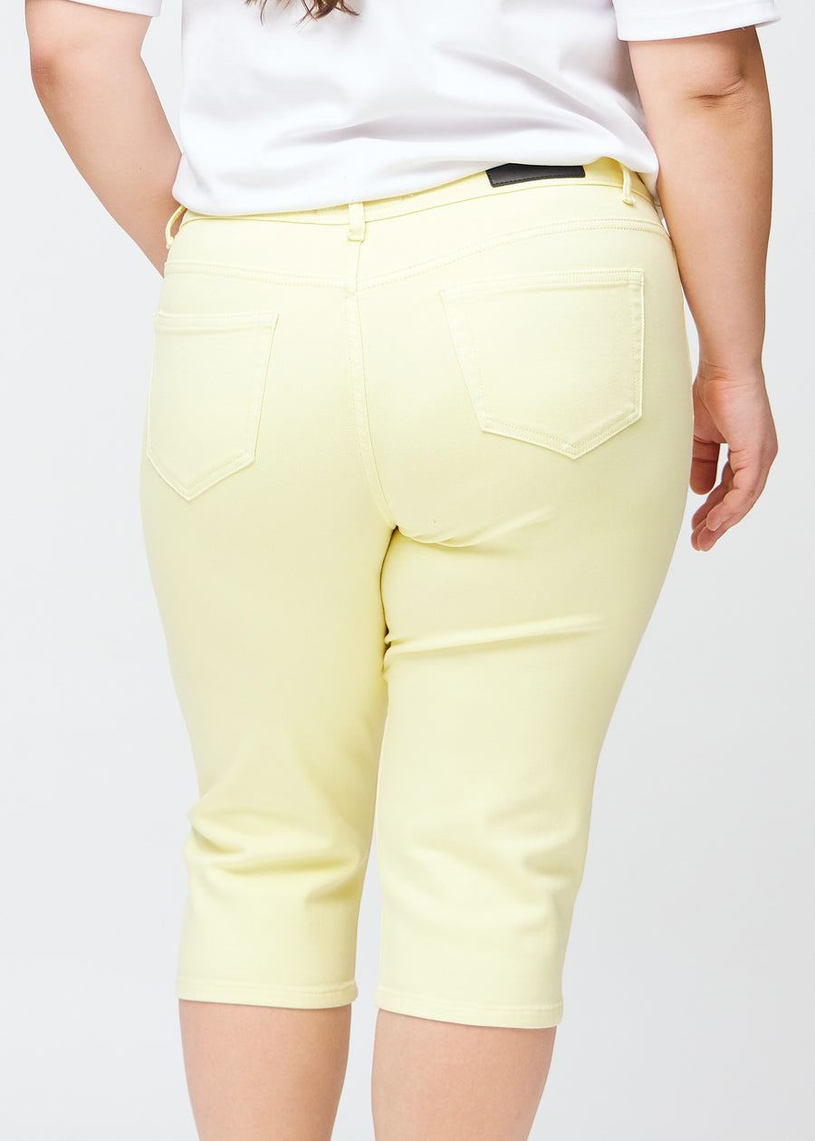 Tæt billede af bagdelen på en plus-size model i lysegule slim capris – detaljefokus på lommer og syninger.