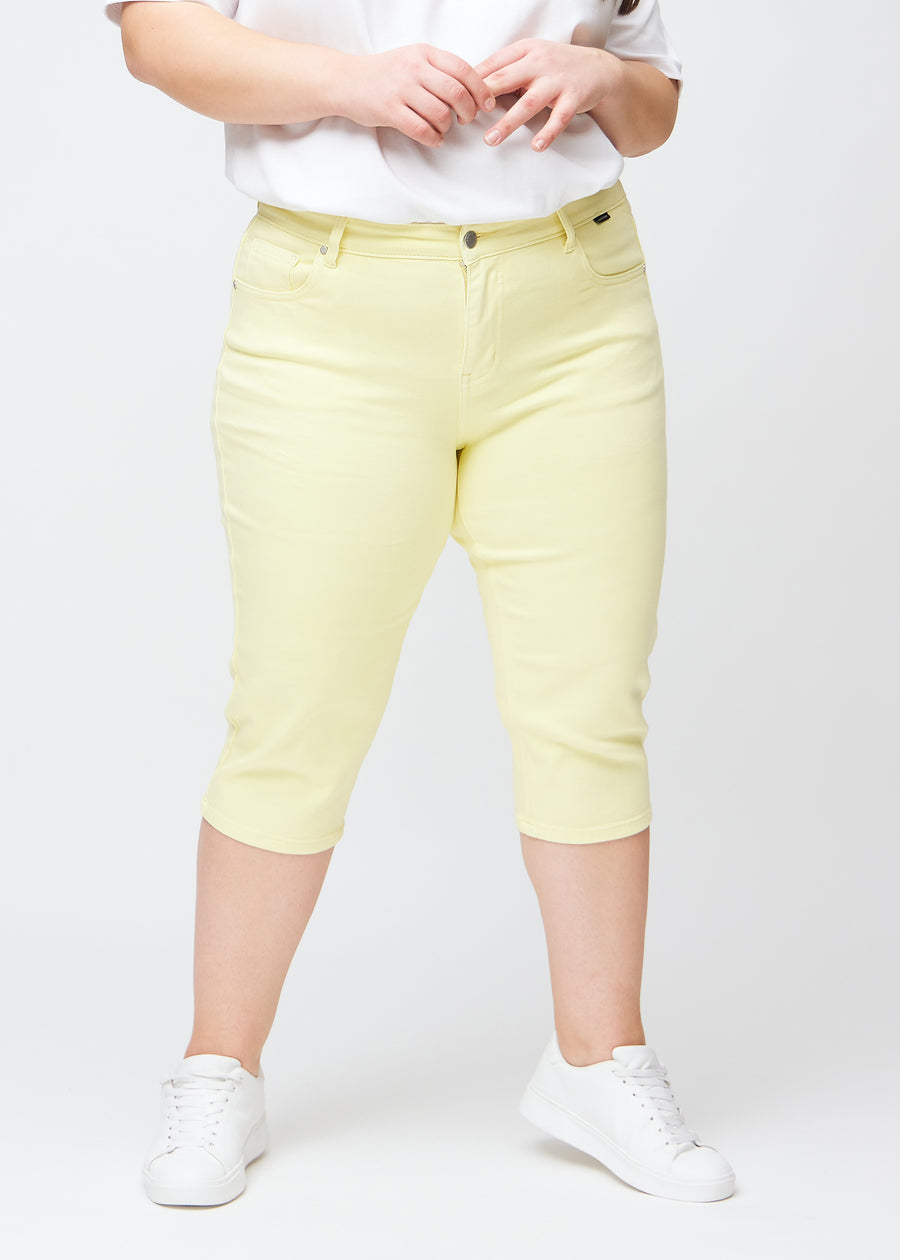 Lysegule slim capris, farve Lemonades, med tætsiddende pasform og længde lige under knæet – set forfra på plus-size model.
