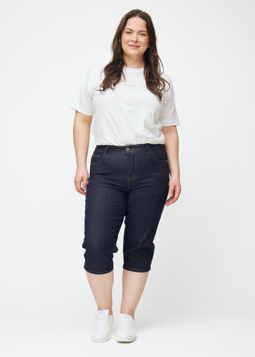 Fuldt billede af plus-size model i dyb mørkeblå denim capris til kvinder i farven Midnights med slim pasform.