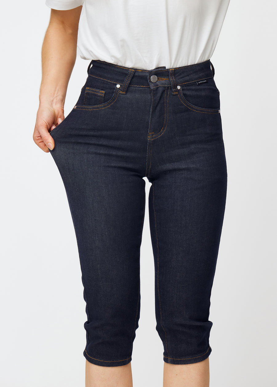 Model strækker dyb mørkeblå denim capris til kvinder i farven Midnights ved låret for at vise materialets stretch.