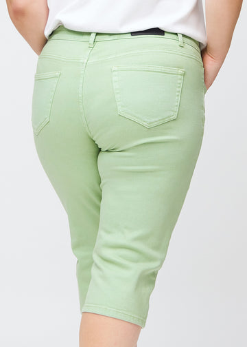 Tæt billede af bagdelen på en plus-size model i lysegrønne slim capris – detaljefokus på lommer og syninger.
