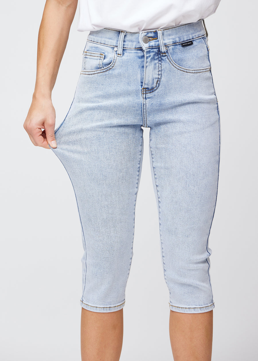 Model strækker caprisene ved låret for at vise det bløde og fleksible stretch i den lyseblå denim.