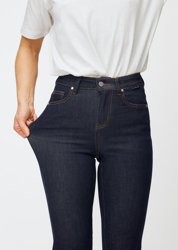 Model strækker dyb mørkeblå denim jeans til kvinder i farven Midnights ved låret for at vise materialets stretch.