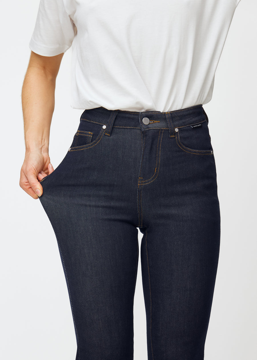 Model strækker dyb mørkeblå denim jeans til kvinder i farven Midnights ved låret for at vise materialets stretch.