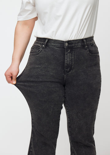 Plus-size model strækker jeansene ved låret for at vise stretch.