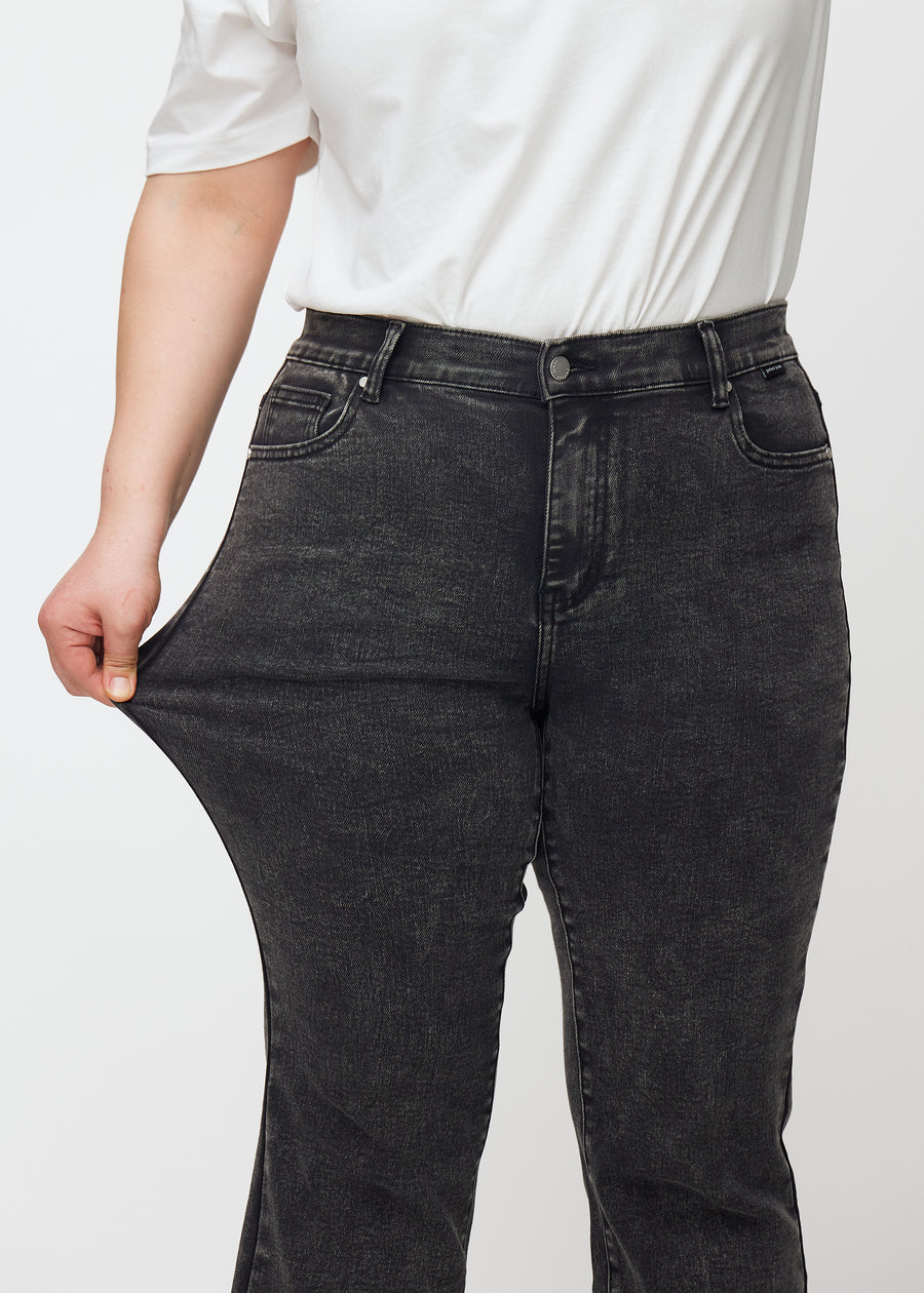 Plus-size model strækker jeansene ved låret for at vise stretch.