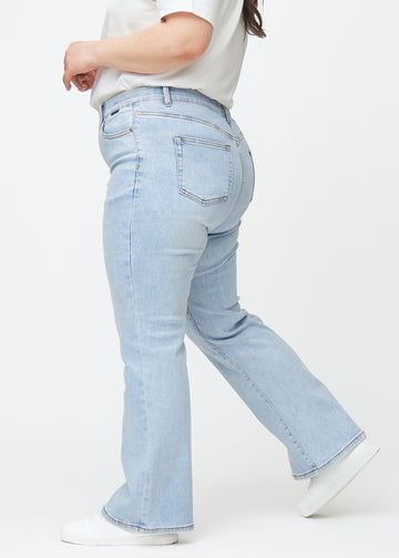 Lyseblå mid-rise bootcut jeans i denimfarven Waves set fra siden på en plus-size model.