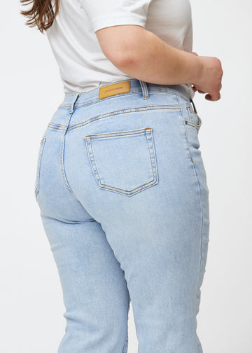 Lyseblå mid-rise bootcut jeans i denimfarven Waves set bagfra tæt på en plus-size model for at vise detaljer.