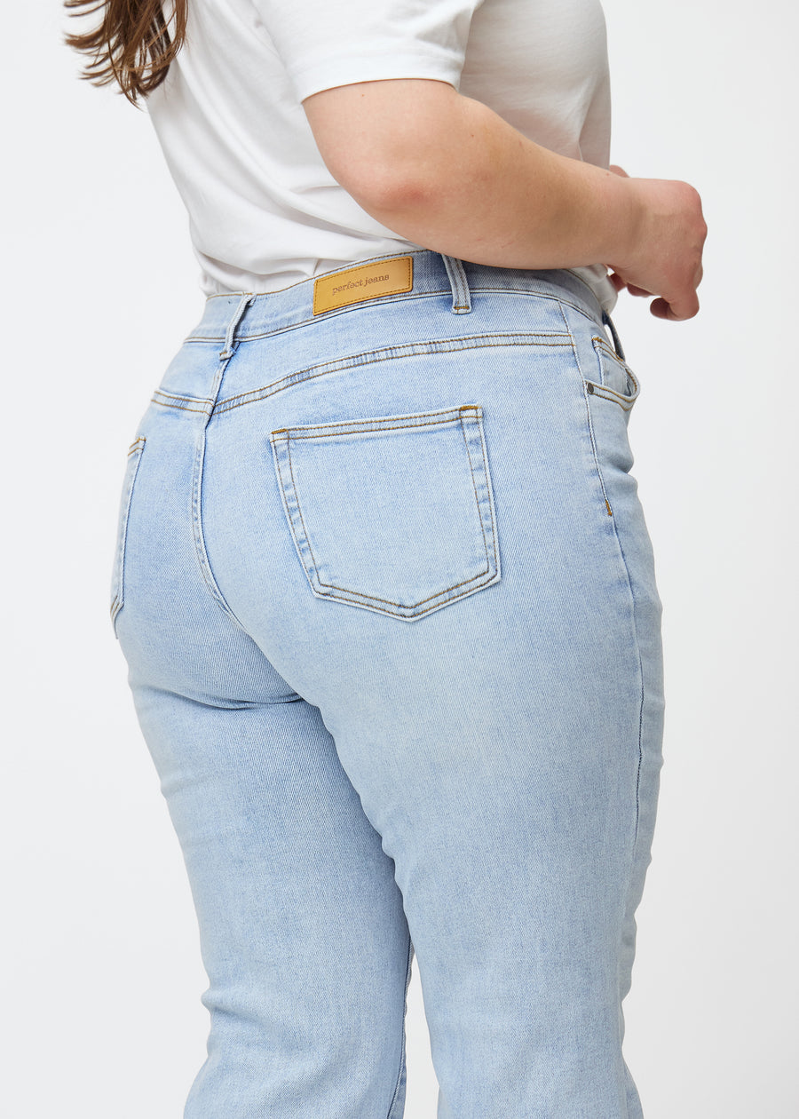 Lyseblå mid-rise bootcut jeans i denimfarven Waves set bagfra tæt på en plus-size model for at vise detaljer.