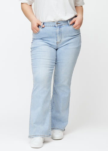 Lyseblå mid-rise bootcut jeans i denimfarven Waves, som sidder tæt fra hofte til lår og har et let svaj forneden, på en plus-size model, set forfra.