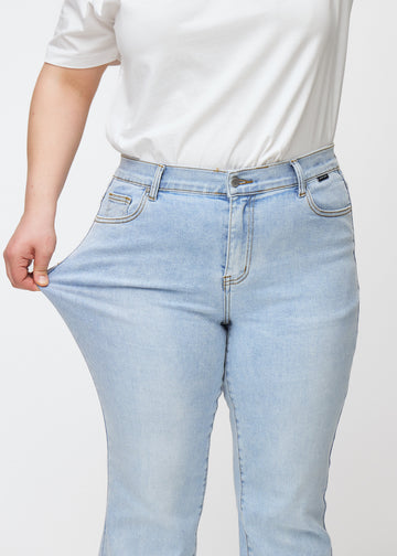 Plus-size model strækker jeansene ved låret for at vise stretch.