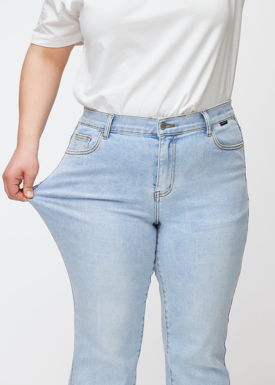 Plus-size model strækker jeansene ved låret for at vise stretch.