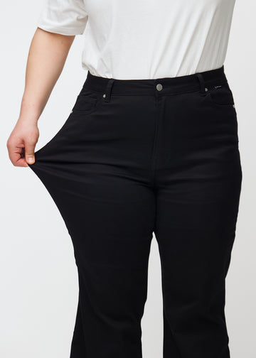 Plus-size model strækker jeansene ved låret for at vise stretch.