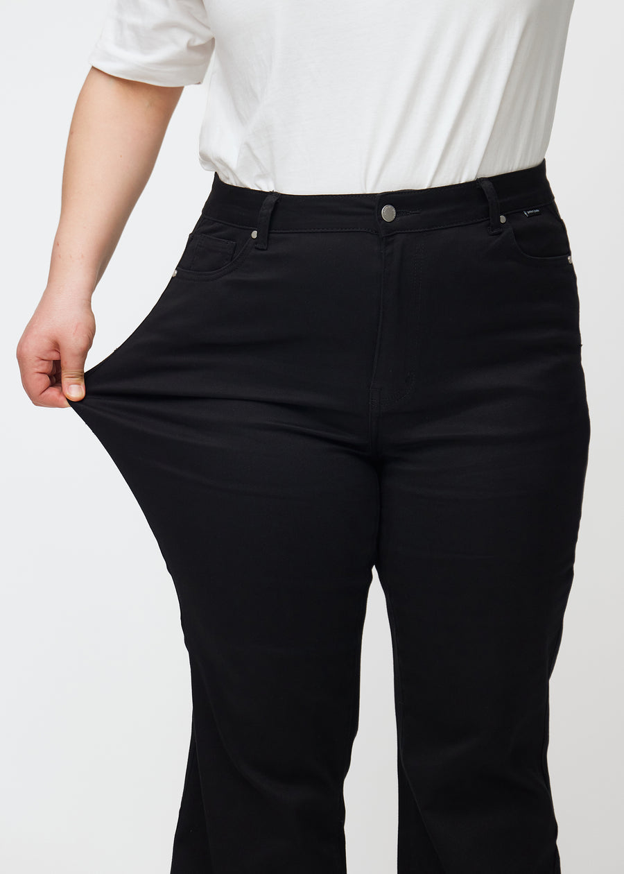 Plus-size model strækker jeansene ved låret for at vise stretch.