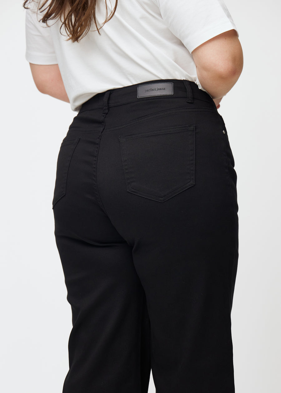 Sorte højtaljede jeans, som sidder til i taljen og har en løs pasform med bredde ned, set tæt på bagfra på en plus-size model for at vise detaljer.